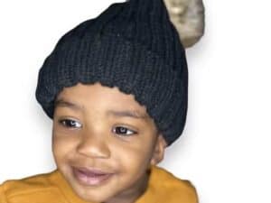 A young child wearing a black hat with a pom-pom.