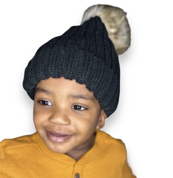 A young child wearing a black hat with a pom-pom.